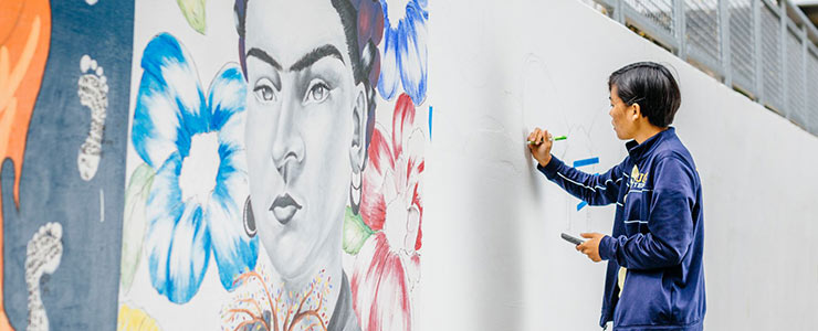 Artist is painting next to Frida Kahlo mural